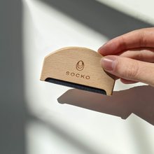 Load image into Gallery viewer, Socko Pilling comb for debobbling your knitwear. care for cashmere. clothing care. wooden handle clothing comb. Hand holding comb with daylight shadows in background. round flat lay.